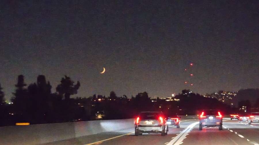 Original nighttime freeway photograph with a crescent moon, hillside lights, communication towers, and traffic.